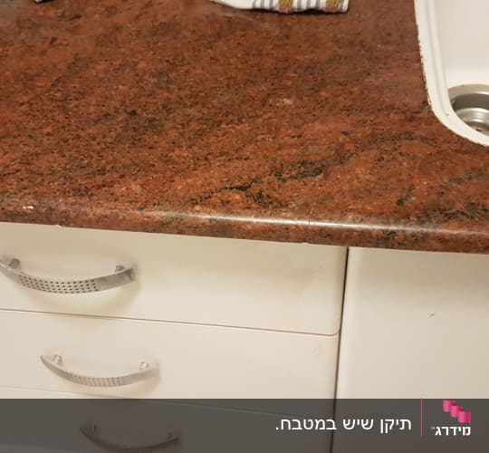 משטח שיש אדום-חום מותקן במטבח עם כיור שקוע